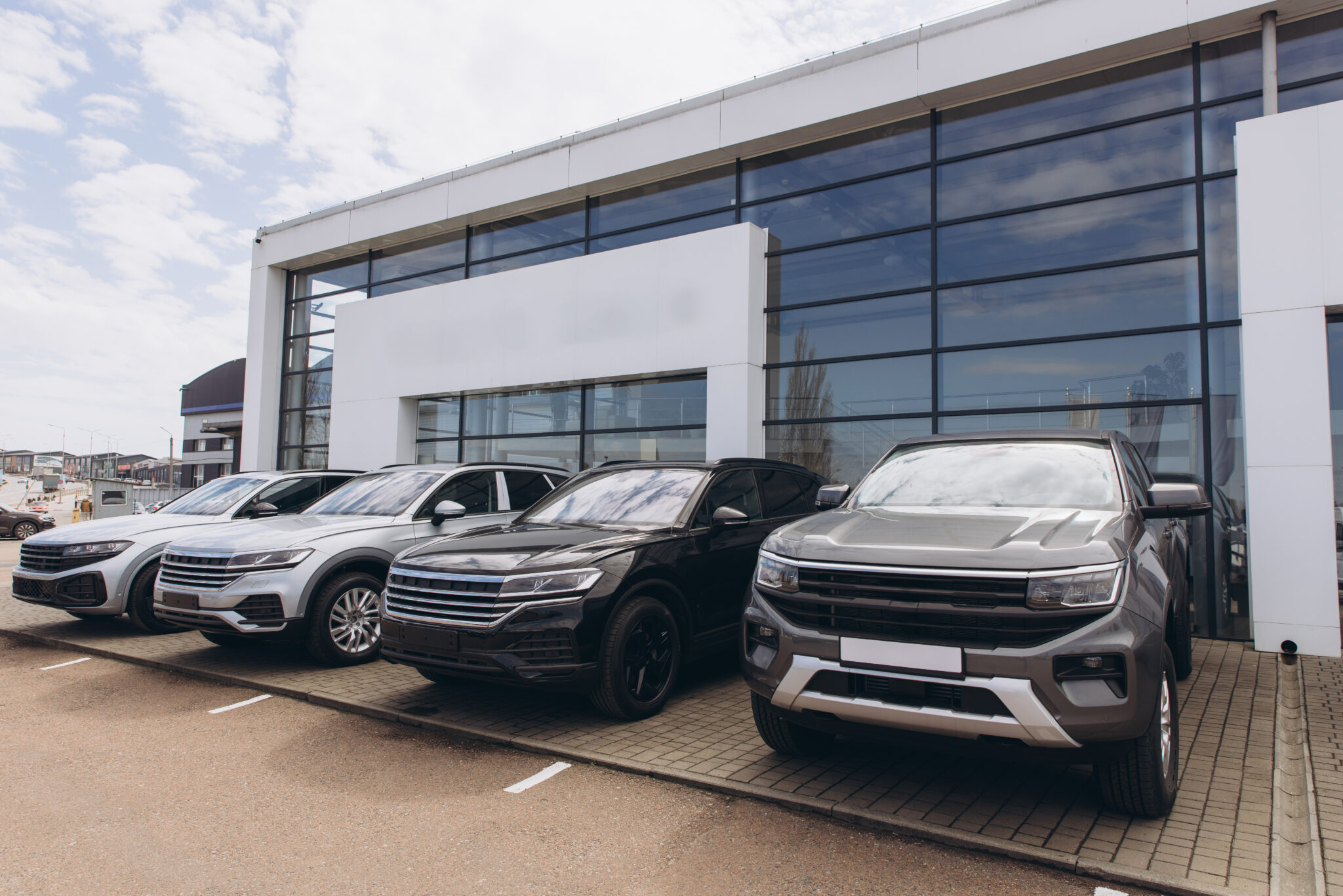Shiny new cars parked in front of a modern car dealership showroom building, ready to be purchased